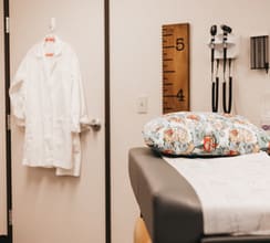A room with a bed, stethoscope and robe hanging on the wall.