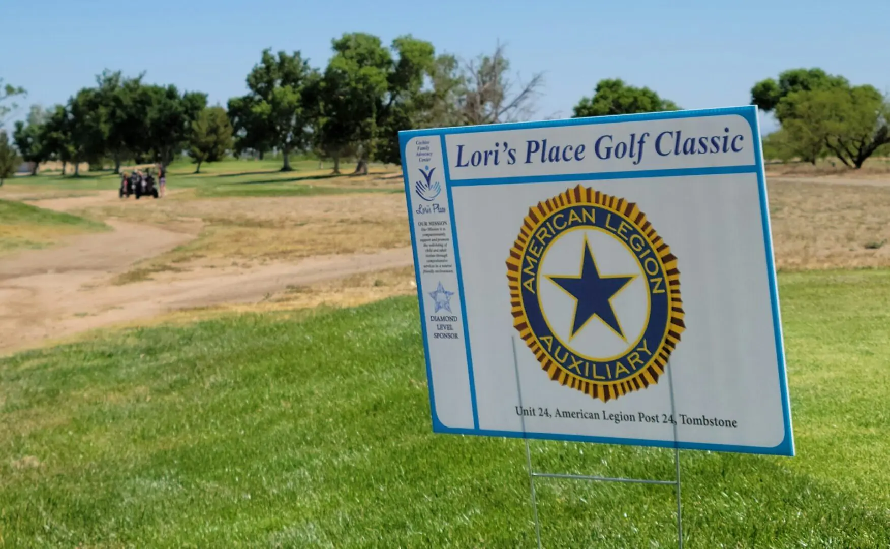 A sign is posted in the grass for lori 's place golf classic.