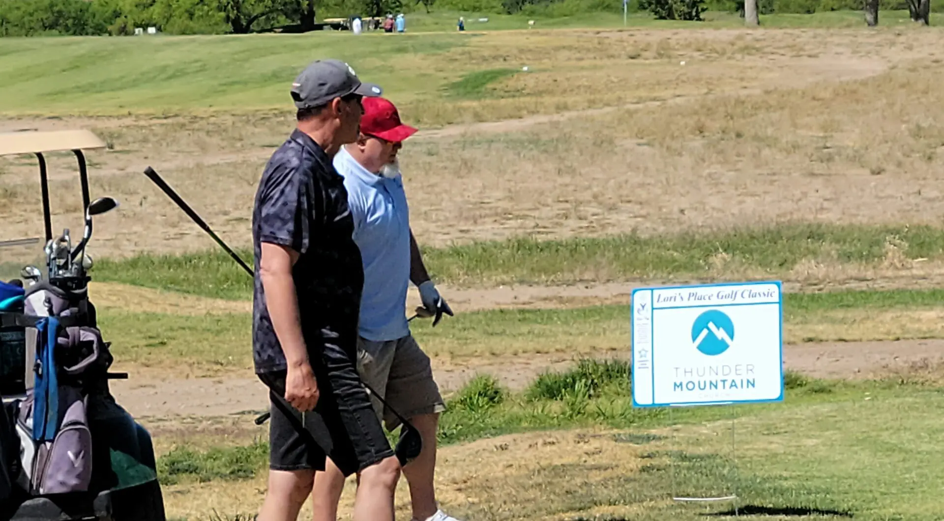 Two men walking across a field holding golf clubs.