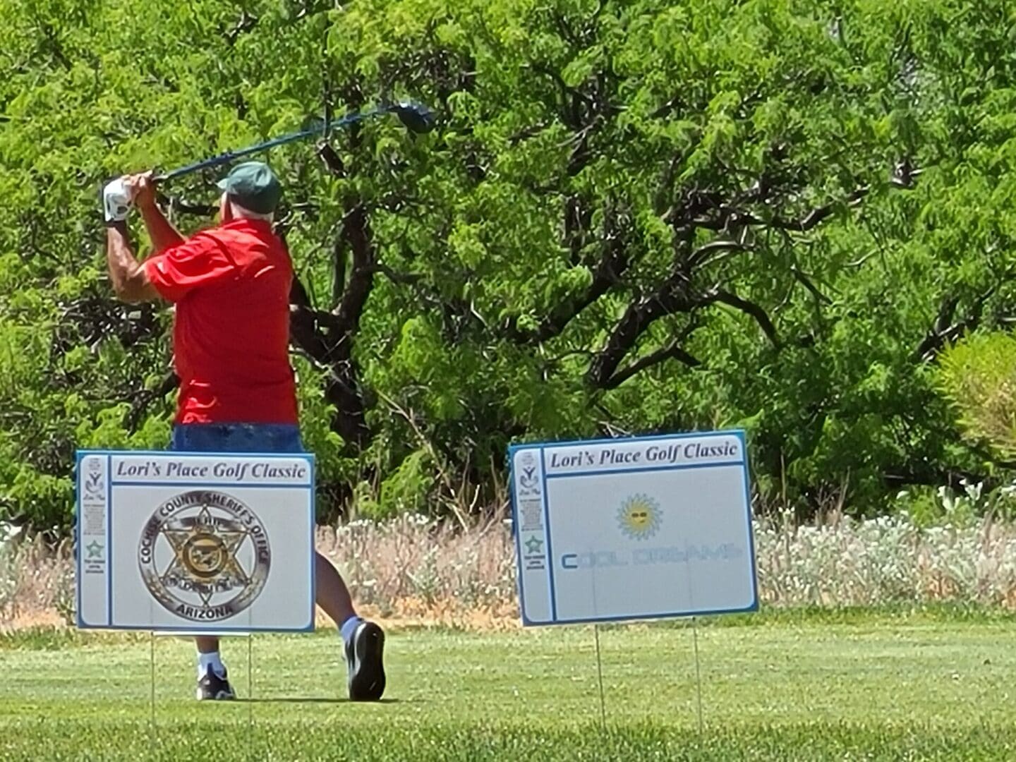 A man in red shirt swinging at a golf ball.