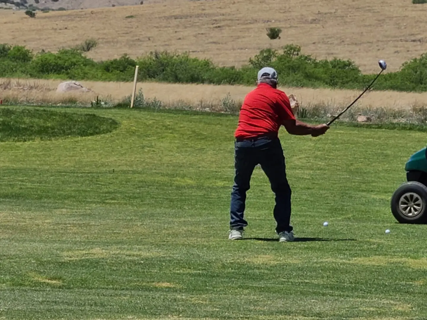A man in red shirt playing golf on green.