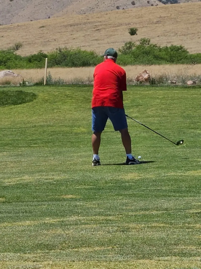 A man in red shirt playing golf on green.
