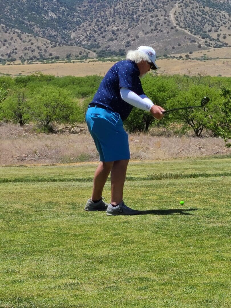 A man in blue shorts and a white hat is playing golf.