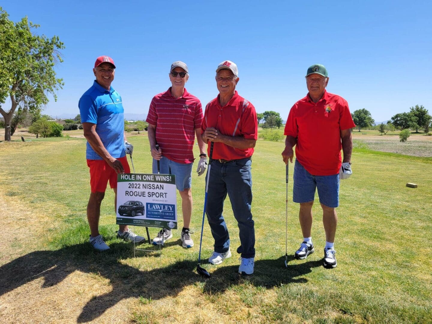 Four men standing on a golf course holding golf clubs.