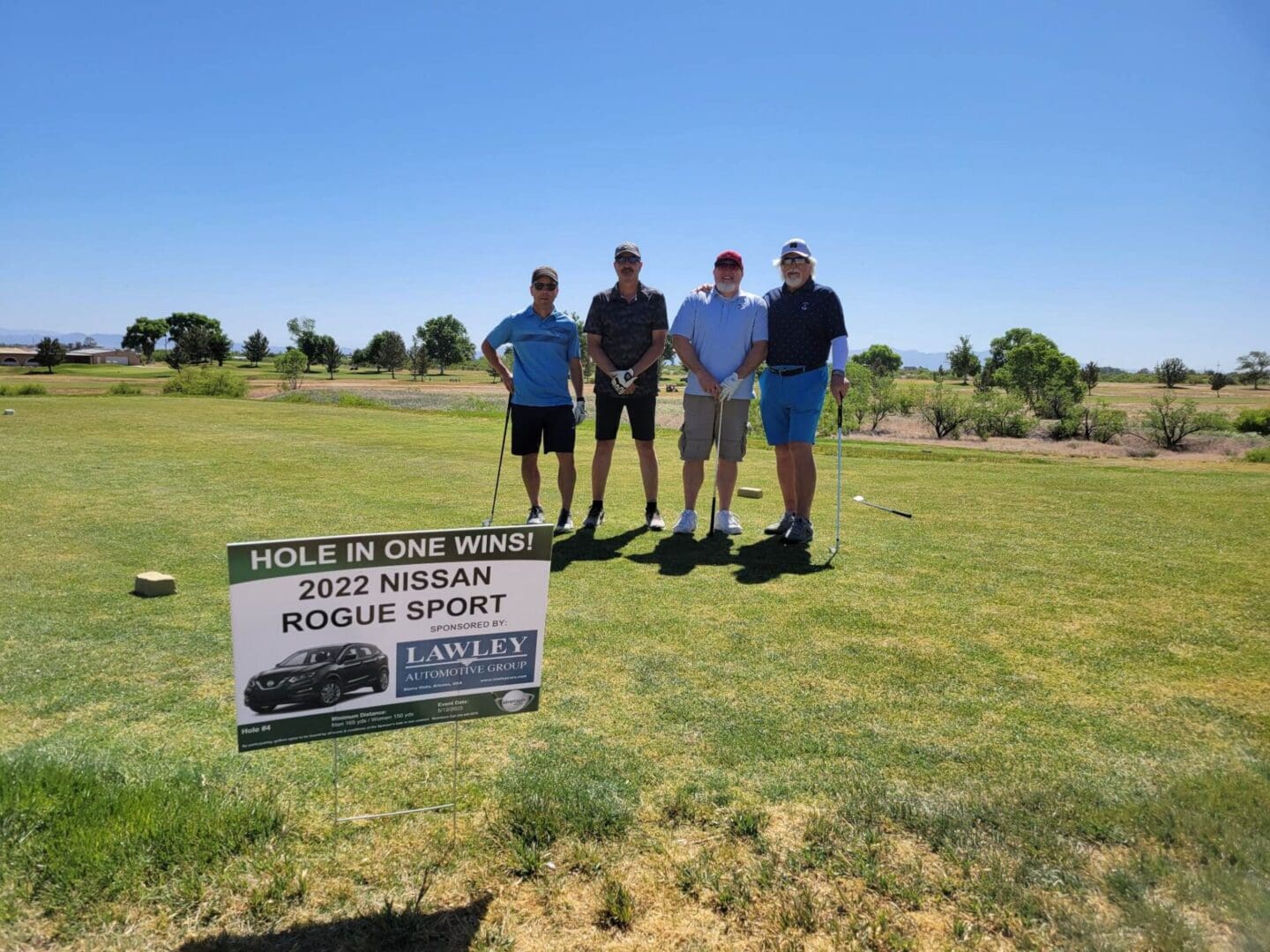 Four men standing on a golf course with a sign.